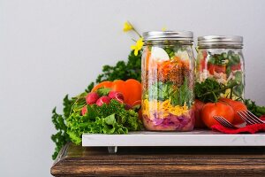 Two layered salads in glass jars with spinach, beans, cheese and eggs