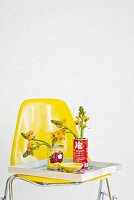 Konservendosen als Blumenvasen auf Tablett und gelbem Stuhl