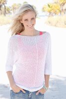 Blonde Frau in weißem Strickpullover, rotem Top darunter und Jeans