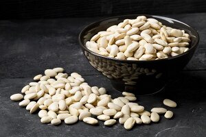 Dried white beans in a bowl and on a black surface