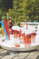 Getränke in Gläsern mit Papierdeckel und Strohhalm auf Gartentisch