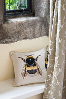Kissen mit Bienenmotiv auf Ablage unter rustikalem Fenster