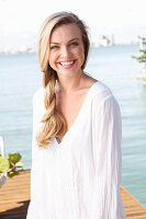 A blonde woman on a jetty wearing a white tunic dress