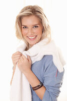 Junge blonde Frau in blauem Pullover mit weisser Kuschelpulli über den Schultern