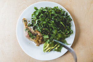 Kale salad with a roasted chicken leg and sliced avocado