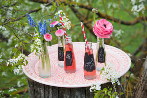 Labelled bottles of pop and flowers on tray in garden