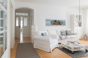 White, loose-covered sofa set, pallet coffee table and pale wooden floor in living room of converted dairy