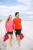 A blonde woman wearing a pink top and a brunette man wearing an orange t-shirt on a beach