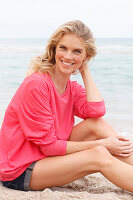 A young blonde woman on a beach wearing a pink top and shorts