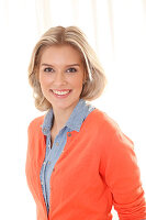 A young blonde woman wearing a denim shirt and an orange cardigan