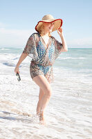 A young blonde woman on a beach wearing a straw hat and a light playsuit