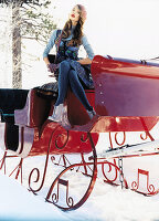 A young woman wearing sitting on a red painted sleigh