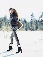 A young woman in the snow wearing jeans, a striped jumper and a faux fur gilet