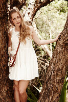 A young woman wearing a white summer dress standing between tree trunks