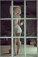 Junge Frau mit rosa Haaren in Spitzen-Slip und oben ohne am Fenster