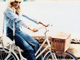 Blonde Frau mit Sonnenbrille in hellblauem Jackett und Jeans auf Fahrrad