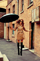 A brunette woman with an umbrella wearing a tench coat, overknee socks and ankle boots