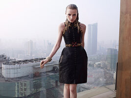 A young woman wearing a black dress in front of a glass balustrade on a skyscraper