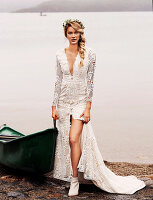 A blonde woman wearing a white wedding dress and a hair wreath by a lake