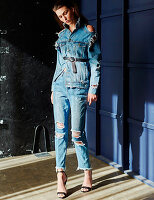 A brunette woman wearing wearing a ripped denim jacket and ripped jeans