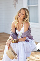 A blonde woman wearing a long, white summer dress with a purple shawl