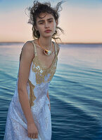 A dark-haired woman wearing a party dress by the sea at sunset