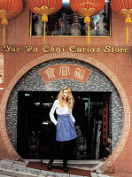 A blonde woman wearing a white blouse and a blue skirt standing outside a Chinese shop