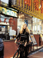 A blonde woman wearing a black dress with a bike outside a Chinese takeaway