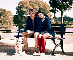 A young couple with a dog sitting on a bench