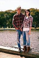 A young couple wearing matching outfits (checked shirts and jeans) standing by a river