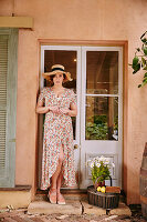 A brunette woman wearing a straw hat and a floral patterned summer dress