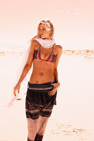 A blonde woman wearing a scarf with a bikini top and summer trousers