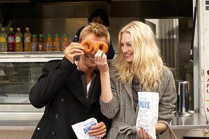 A couple in front of a Food Truck with a man with doughnuts in front of his eyes