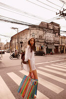 Junge Frau in weißem Tunikakleid mit Einkaufstasche