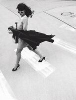 Dunkelhaarige Frau im Kleid und mit Cape in der Hand auf der Straße (s-w-Aufnahme)