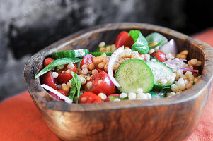Israeli couscous salad with cucumbers, tomatoes and fresh basil in a wooden bowl