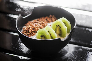 Yogurt with granola and kiwi in a black bowl