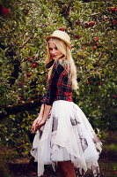 A blonde woman wearing a checked jacket and a tulle skirt by an apple tree