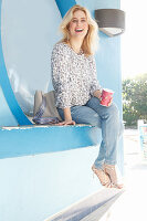 Blonde Frau in Langarmbluse und Jeans sitzt an Strandcafe