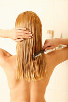 A blonde woman combing conditioner through damp hair