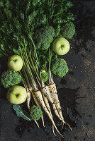 A bunch of parsley, broccoli florets and green apples on dark background