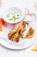 Lemony Marinated Chicken Skewers on a white plate, served with sesame seeds, orange pieces and fresh herbs