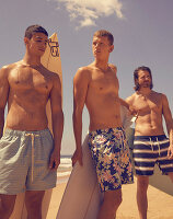 Three young men wearing bathing shorts with surfboards