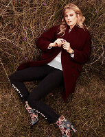 A blonde woman wearing a dark red coat, jeans and floral patterned ankle boots