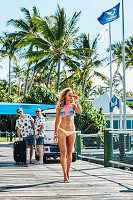 A young woman wearing a bikini with two men in the background wearing Hawaiian shirts