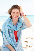 A young woman wearing a denim shirt with a blue jumper over her shoulders