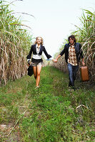 A young woman and a young man with a guitar and a suitcase walking along a field path