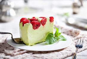 Ein Stück Pistazienmoussetorte mit frischen Himbeeren