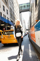 A young blonde woman wearing a black-and-white star hoodie, a gilet and jeans