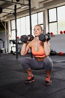 A young woman performing a thruster with dumbbells